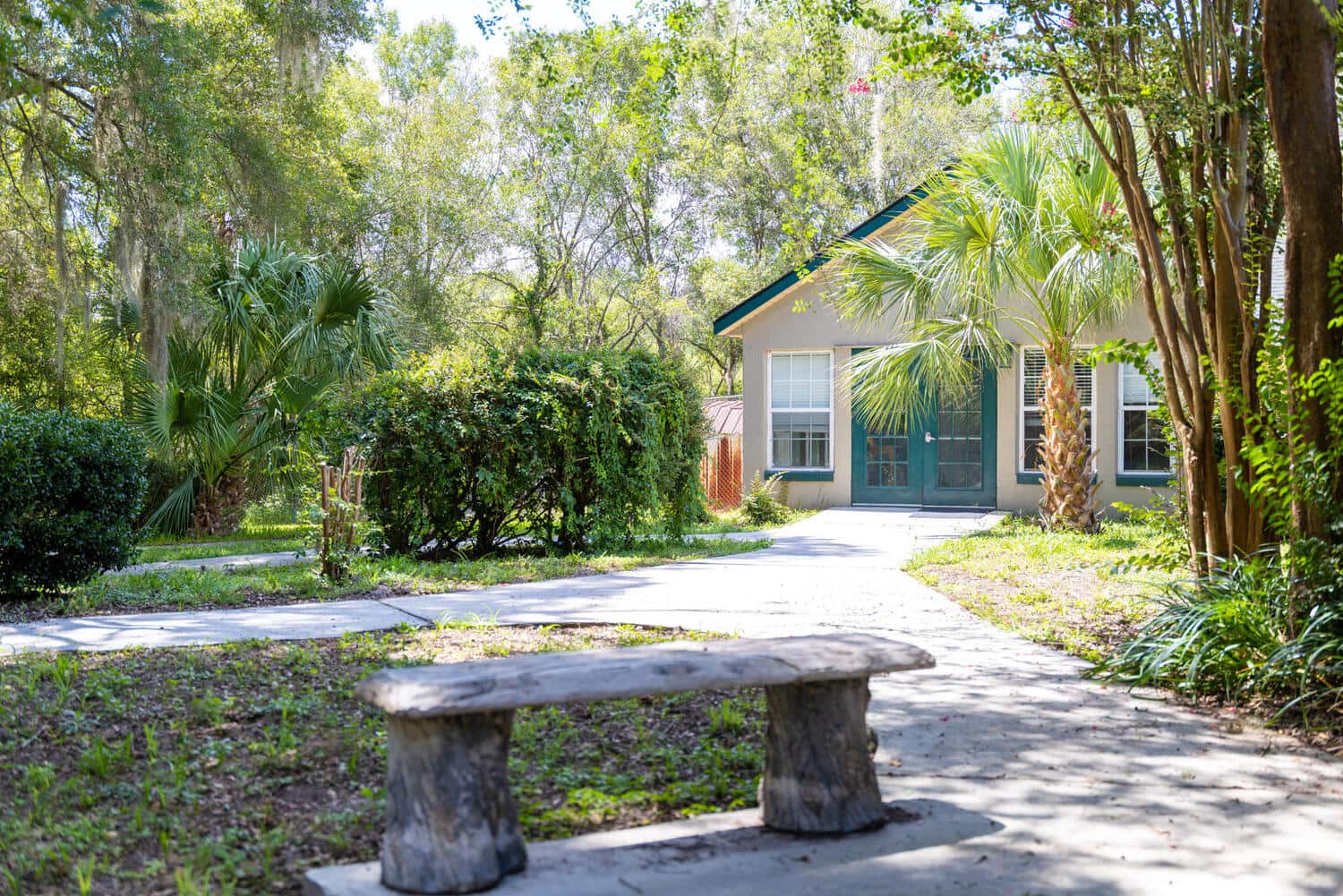 A shaded walking path curving past palms and a cottage with green trim at The Gardens