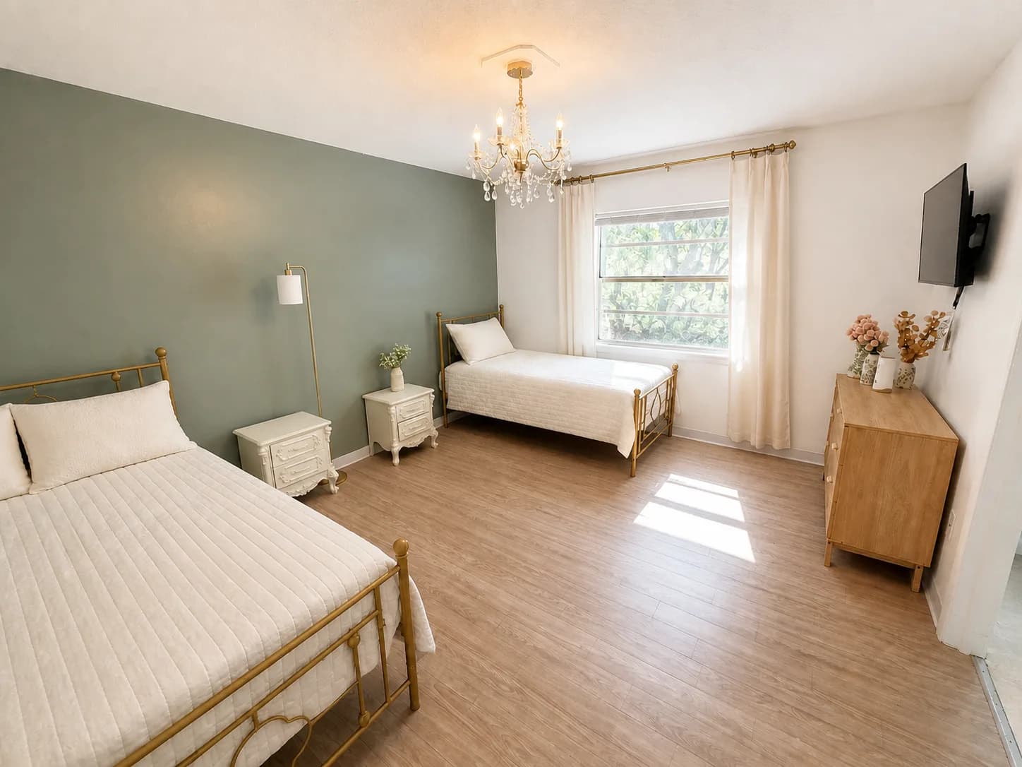 A shared room at The Gardens with two beds, a soft green wall and a chandelier